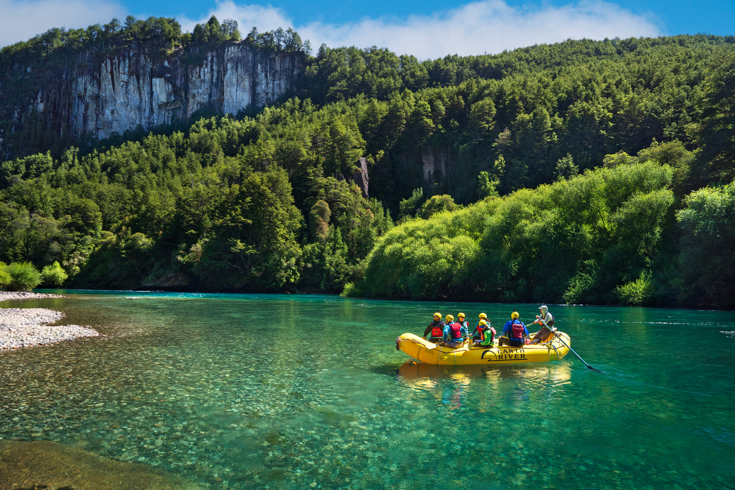 Raft floating through clear turquoise water on the Futaleufú River surrounded by Patagonia forest and cliffs